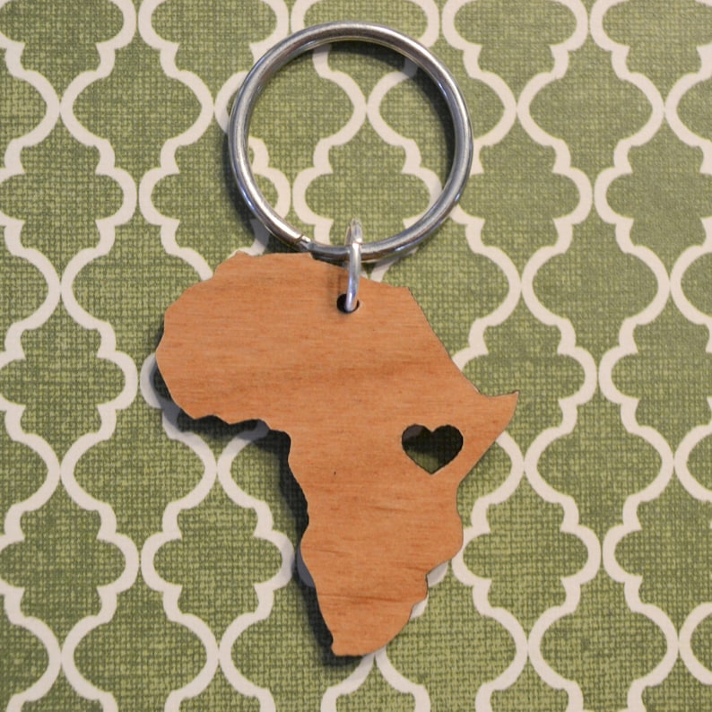 May include: A wooden keychain shaped like the continent of Africa with a small heart cutout in the center. The keychain is attached to a silver key ring.