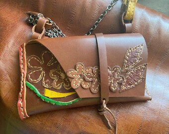 May include: A brown leather purse with a chain strap and floral embroidery. The flowers are stitched in yellow, green, and brown thread.