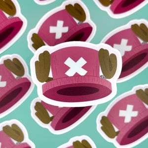 May include: A pink and white hat with a white X on the front and brown ears on the sides. The hat is a popular character from the anime series One Piece.