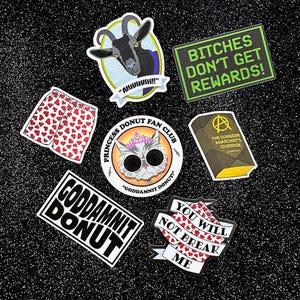 May include: A collection of stickers with various designs and text. Includes a goat with the text "AHHHHHHH!", a pair of shorts with heart patterns, and a cat wearing sunglasses with the text "GODDAMNIT DONUT!". Other stickers say "BITCHES DON'T GET REWARDS!" and "YOU WILL NOT BREAK ME".