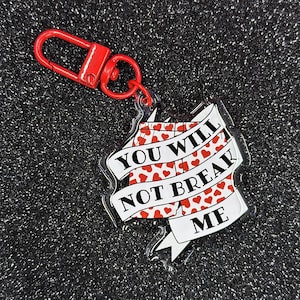 May include: A red and white acrylic keychain with a pair of red underwear with white hearts printed on them. The underwear has a white banner that says "You Will Not Break Me".