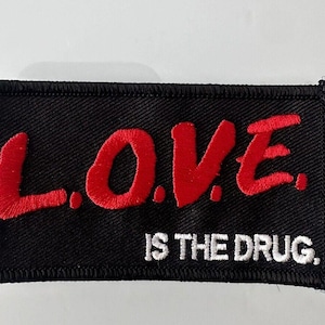 May include: Black embroidered patch with red lettering that reads "LOVE. IS THE DRUG."