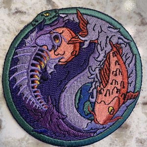 May include: Embroidered patch with a purple and orange dragon and a red and orange fish, both swimming in a circle with a green border.