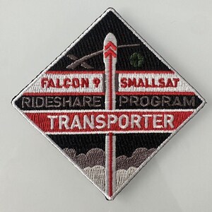 Peut inclure: Un écusson en forme de losange noir et blanc avec du texte rouge et blanc. Le texte indique "Falcon 9 SmallSat Rideshare Program Transporter". Une fusée blanche avec des rayures rouges se trouve au centre de l'écusson.