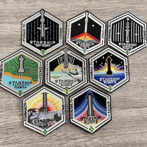 Puede incluir: Una colección de parches hexagonales bordados con el cohete Starship de SpaceX. Cada parche muestra un diseño único, incluyendo el cohete despegando, con texto como "Starbase TX" y "Starship Flight". Los parches son de varios colores, incluyendo negro, azul y naranja.