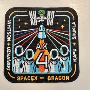 Puede incluir: Parche bordado que representa un lanzamiento de cohete con estelas coloridas, el número 4 y astronautas. El parche incluye el texto "SPACEX - DRAGON" y los nombres de los miembros de la tripulación. El diseño está sobre un fondo negro con un borde.