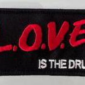 May include: Black embroidered patch with red lettering that reads "L.O.V.E. IS THE DRUG."