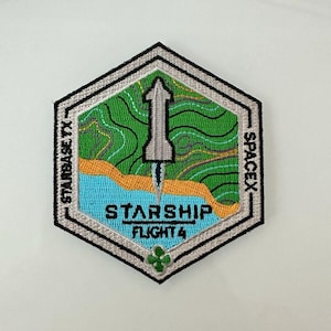 Puede incluir: Un parche hexagonal con un contorno blanco y costuras negras. El parche presenta una nave espacial estilizada en plata con un paisaje verde y azul detrás. El texto "STARBASE TX" está en el lado izquierdo del parche y "SPACEX" está en el lado derecho. El texto "STARSHIP FLIGHT 4" está en el centro del parche.