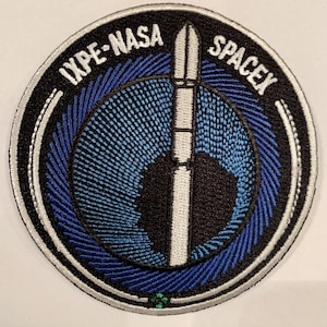 May include: Embroidered patch featuring the text "IXPE-NASA SPACEX" in white on a black background. The patch has a blue and black design with a white rocket in the center. The patch is circular with a white border.