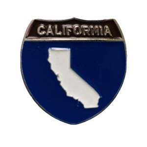 May include: A blue and white California state highway sign-shaped pin. The pin features the word "CALIFORNIA" in silver lettering at the top, with a white outline of the state on a blue background.