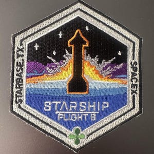 Puede incluir: Parche bordado con un diseño de lanzamiento de cohete negro, naranja y blanco. El parche presenta el texto "STARBASE TX" y "SPACEX" en los lados, con "STARSHIP FLIGHT 8" en el centro. El parche tiene forma hexagonal con borde blanco.