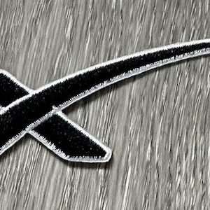 May include: Black and white embroidered patch with a stylized 'X' and a curved line, resembling a rocket ship.