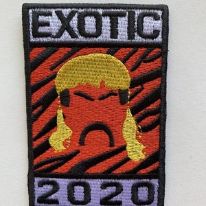 May include: Embroidered patch with the word "EXOTIC" above a stylized face and the number "2020". The patch features a red background with black tiger stripes, a yellow hairstyle, and purple text.