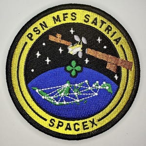 Può includere: Un cerotto circolare nero e giallo con il testo "PSN MFS SATRIA SPACEX" attorno al bordo. Il centro del cerotto presenta un satellite in orbita attorno a un globo blu e verde con una rete bianca di linee. Il globo è circondato da uno sfondo nero con stelle bianche.
