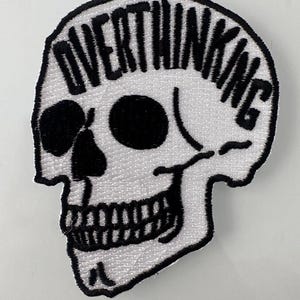 May include: White embroidered skull patch with the word "OVERTHINKING" in black lettering around the top of the skull.