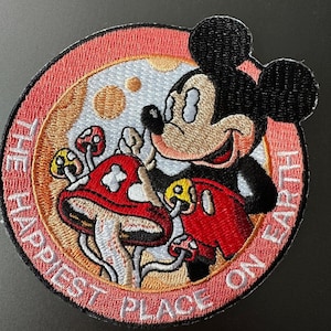 May include: Embroidered patch featuring Mickey Mouse holding a red mushroom with the text "The Happiest Place on Earth" in a pink circle.