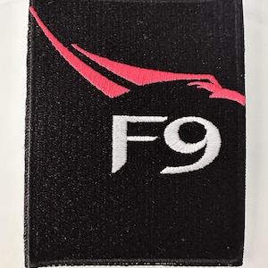 Puede incluir: Parche bordado negro con un cohete rojo y el texto "F9" en blanco.