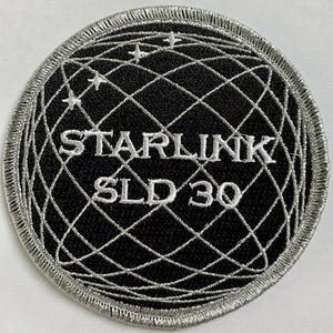 以下が含まれることがあります： 「Starlink SLD 30」という文字と、線と星で描かれた地球のデザインが施された、黒と銀の刺繍パッチです。