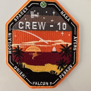May include: A black and orange embroidered patch with the text "SPACEX", "NASA", "CREW - 10", "FALCON 9", "MCCLAIN", "ONISHI", "AYERS", and "PESKOV". The patch features a sunset scene with a comet, palm trees, and a space station.