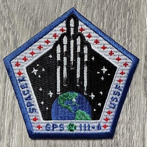 May include: A blue and white embroidered patch with a black background. The patch features a rocket launch with the text "SPACEX GPS III-6 USSF" around the edge.