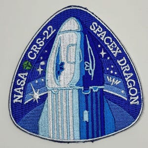 May include: A blue and white embroidered patch with the text "NASA CRS-22 SPACEX DRAGON" and a white silhouette of a rocket ship.
