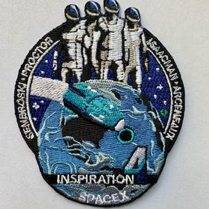 May include: A blue and white embroidered patch featuring four astronauts standing on a blue and white globe. The globe is encircled by a blue ring with white stars and the text "Inspiration4 SpaceX" and the names of the astronauts: "Sembroski, Proctor, Isaacman, Arceneaux".