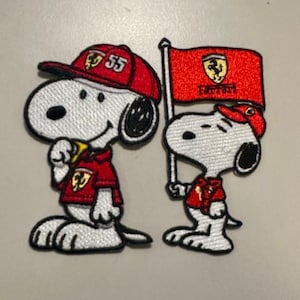 May include: Two embroidered patches featuring Snoopy in red Ferrari attire. One patch shows Snoopy wearing a red cap with the number 55, and a red shirt. The other patch shows Snoopy holding a red Ferrari flag.