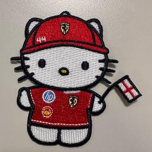 Op de afbeelding: Geborduurde patch met een cartoonkat die een rode baseballcap met het nummer 44 en een rood shirt draagt. De kat houdt een kleine vlag vast met een witte achtergrond en een rood kruis.