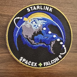 May include: Embroidered patch with the text "STARLINK" at the top and "SPACEX FALCON 9" at the bottom. The patch features a blue and yellow design with a stylized image of the Earth and a satellite. The patch has a black background and a gold border.