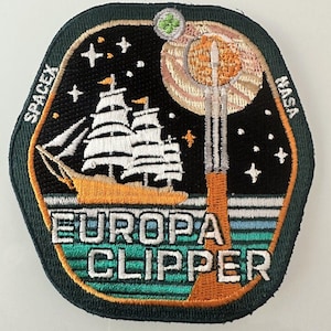 May include: Embroidered patch featuring a stylized design with a sailing ship, a rocket launching, and the text "EUROPA CLIPPER." The patch includes the SpaceX and NASA logos, set against a starry night sky with a planet and a green and white design.