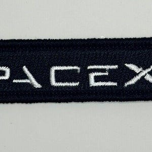 Puede incluir: Un parche bordado negro con el texto blanco "SpaceX" y una nave espacial estilizada blanca.