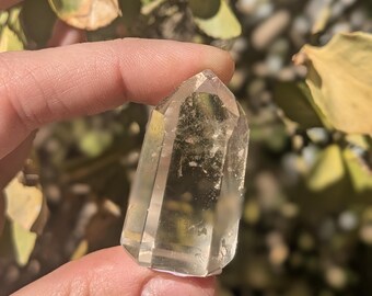 May include: A clear quartz crystal point with a light brown hue. The crystal is pointed at the top and has a flat base.