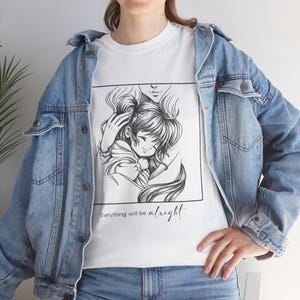Puede incluir: Camiseta blanca con una ilustración en blanco y negro de estilo anime de un niño abrazado. El texto "Everything will be alright" está impreso debajo. La persona lleva una chaqueta vaquera azul claro.