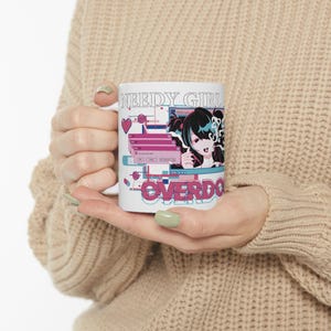Puede incluir: Una taza de cerámica blanca con un estampado gráfico que incluye el texto NEEDY GIRL OVERDOSE. El diseño presenta un personaje de anime estilizado, ventanas emergentes rosas y varios iconos digitales en tonos rosa, azul y negro sobre fondo blanco.