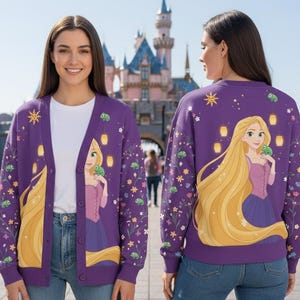 Op de afbeelding: Een paarse cardigan en sweatshirt set met een prinsessenontwerp. De cardigan heeft een knoopsluiting aan de voorkant en een prinsessenafbeelding op de voorkant. De sweatshirt heeft een bijpassend ontwerp op de achterkant. De set is versierd met bloemen en lantaarns.