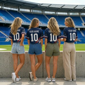 May include: Four individuals seen from behind wearing matching navy blue sports jerseys with white text reading YOUR NAME and the number 10 on the back. The jerseys feature red and white accents on the sleeves. They are standing in a stadium.
