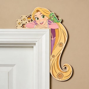 May include: Wooden door frame decoration featuring a cartoon princess with long blonde hair, a green chameleon, and decorative suns. The princess is wearing a pink and purple dress. The decoration is designed to fit over a door frame.