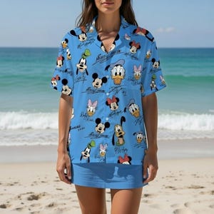 Może przedstawiać: Jasnoniebieska koszula zapinana na guziki i pasująca spódnica z wzorem Myszki Miki, Myszki Minnie, Kaczora Donalda, Kaczki Daisy, Goofy'ego i Pluto. Koszula ma krótkie rękawy i kołnierzyk. Postacie są w różnych pozach ze swoimi podpisami.