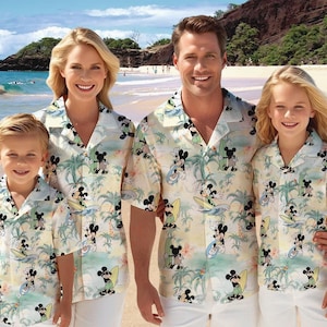 May include: A family of four wearing matching white and yellow Hawaiian shirts with a Mickey Mouse surfing design. The shirts feature palm trees, waves, and Mickey Mouse characters.