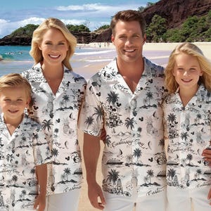 May include: A family of four wearing white short-sleeved shirts with a black and white tropical print. The shirts feature a Mickey Mouse design and the text "Castaway Cay". The family is standing on a beach.