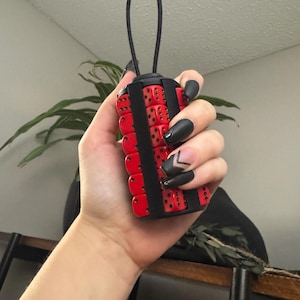 May include: A black and red dice keychain with a loop for attaching to a bag or belt. The keychain is made of multiple dice that are connected together.