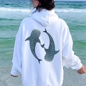 Könnte beinhalten: Weißer Hoodie mit einem Aufdruck von zwei Walhaien, die mit einem Herzen dazwischen schwimmen.