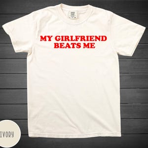 May include: Ivory t-shirt with red text that reads "My Girlfriend Beats Me."