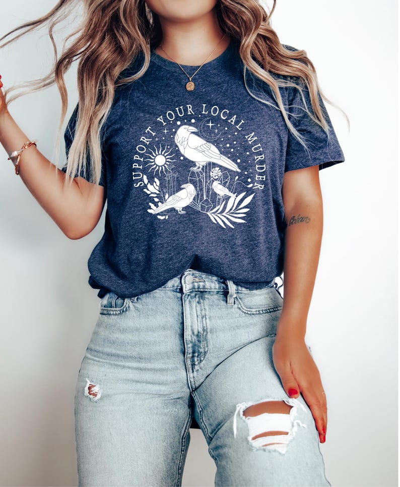 May include: A navy blue t-shirt with a white graphic design featuring three ravens, a sun, and the text "Support Your Local Murder".