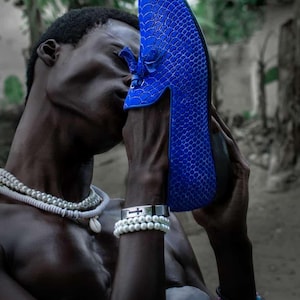 Könnte beinhalten: Ein leuchtend blauer Schuh mit einem strukturierten, schuppenartigen Muster. Der Schuh wird hochgehalten, um sein Design zu zeigen. Der Hintergrund ist unscharf.