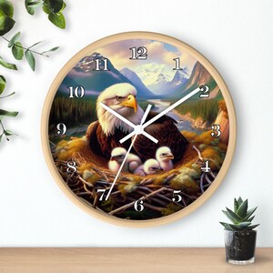 May include: A round wall clock with a wood frame and a white face. The clock features a painting of a bald eagle with its young in a nest. The numbers 1 through 12 are printed in white around the clock face.