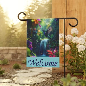 May include: A garden flag featuring a vibrant illustration of a hummingbird in flight near a waterfall, surrounded by lush greenery and colorful flowers. The word "Welcome" is displayed on a light blue banner at the bottom of the flag.