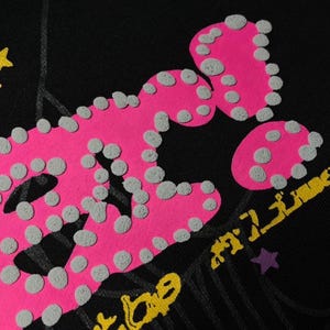 May include: Black fabric with a large, textured pink graphic and gray dots. Yellow and purple accents are visible, along with the partial text "TIME". The design has a distressed, vintage aesthetic.