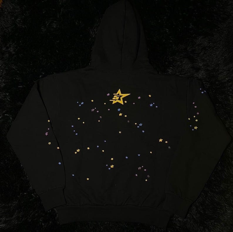 May include: Black hooded sweatshirt with a star design. The back of the sweatshirt features a gold star graphic and scattered smaller stars in yellow, blue, and purple. The sweatshirt has a drawstring hood and a kangaroo pocket.