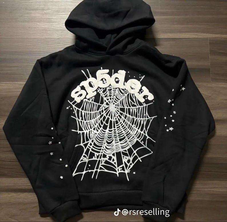 Puede incluir: Sudadera con capucha negra con un dise&ntilde;o de telara&ntilde;a blanca y la palabra "sp5der" en una fuente estilizada. Acentos de estrellas blancas en las mangas. La sudadera tiene un bolsillo delantero y una capucha con cord&oacute;n.